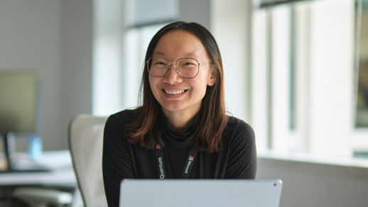 Person sitting at a desk using a laptop in a modern office with large windows in the background