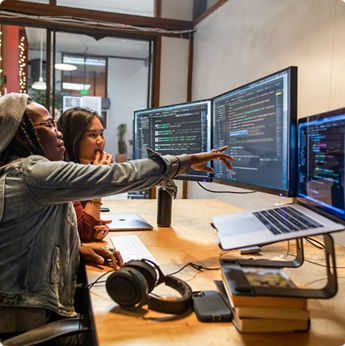 Two people collaborating pointing at code on dual monitors 