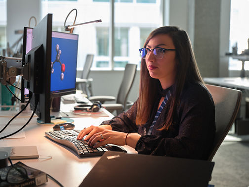 Person working at dual monitors with a molecular model on screen