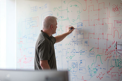 Person writing diagrams and equations on a whiteboard filled with technical sketches